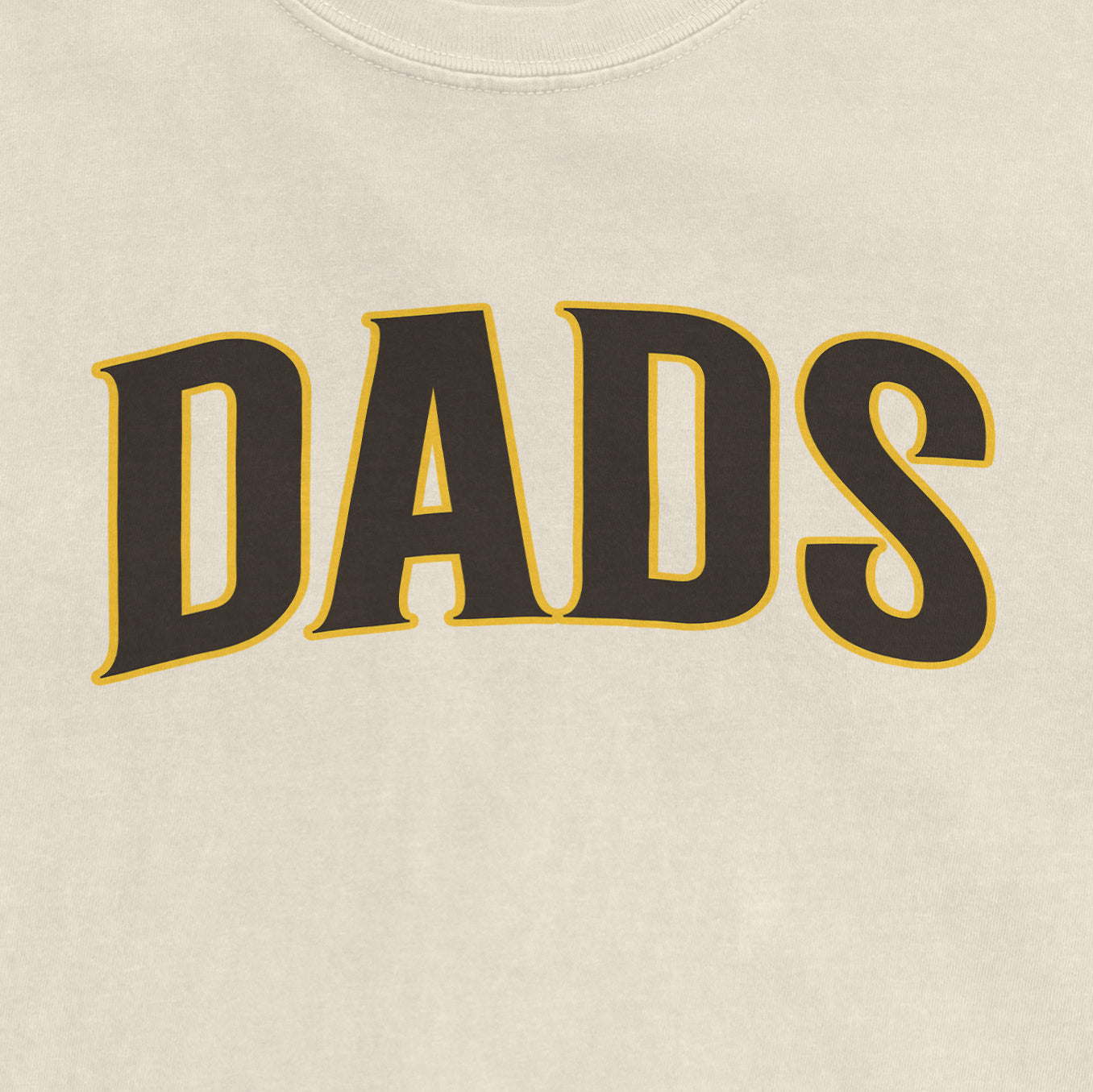 Close-up of a beige T-shirt with the word "DADS" printed in bold black letters outlined in yellow.