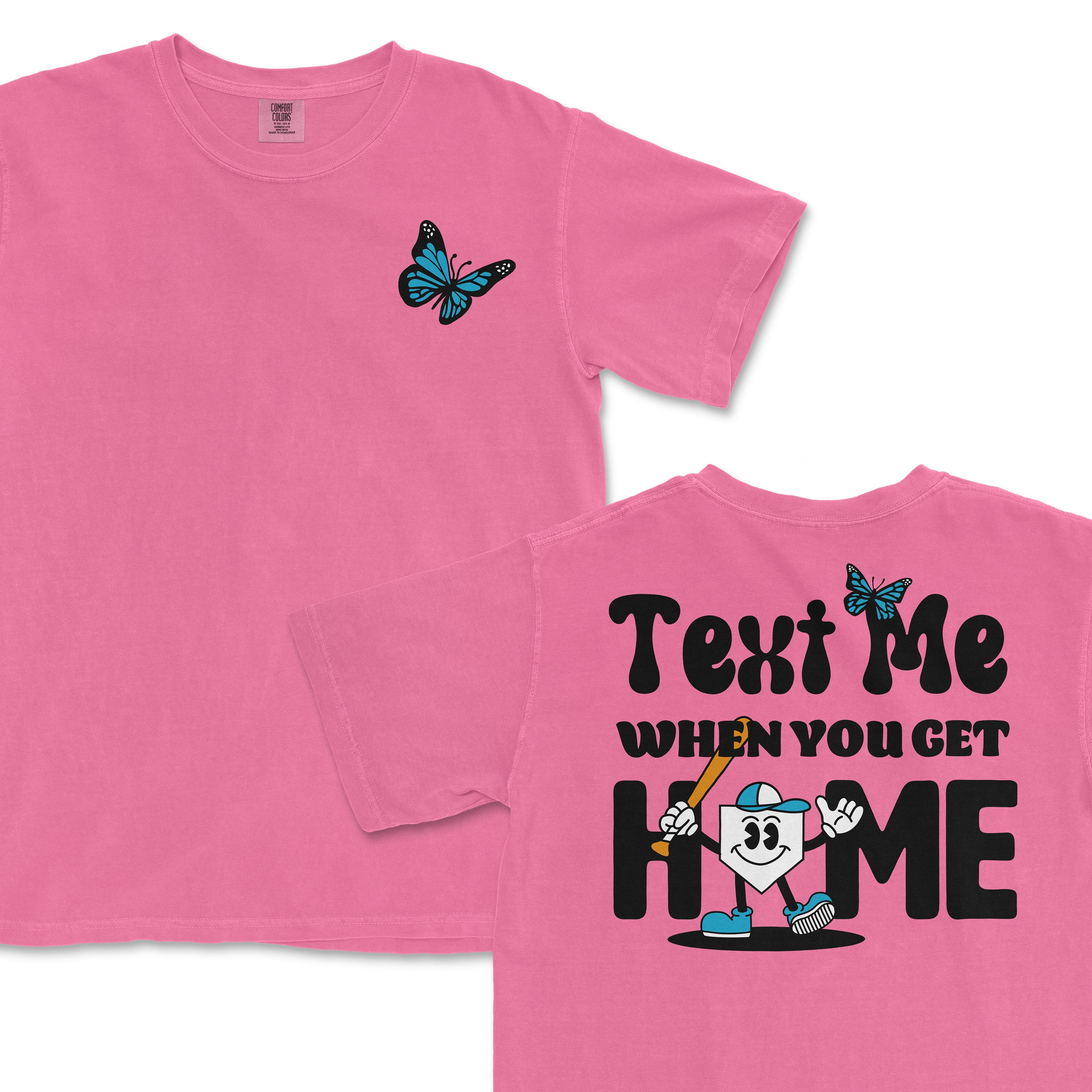 Pink T-shirt with a blue butterfly on the front and a cartoon character holding a bat on the back, with the text "Text me when you get home.
