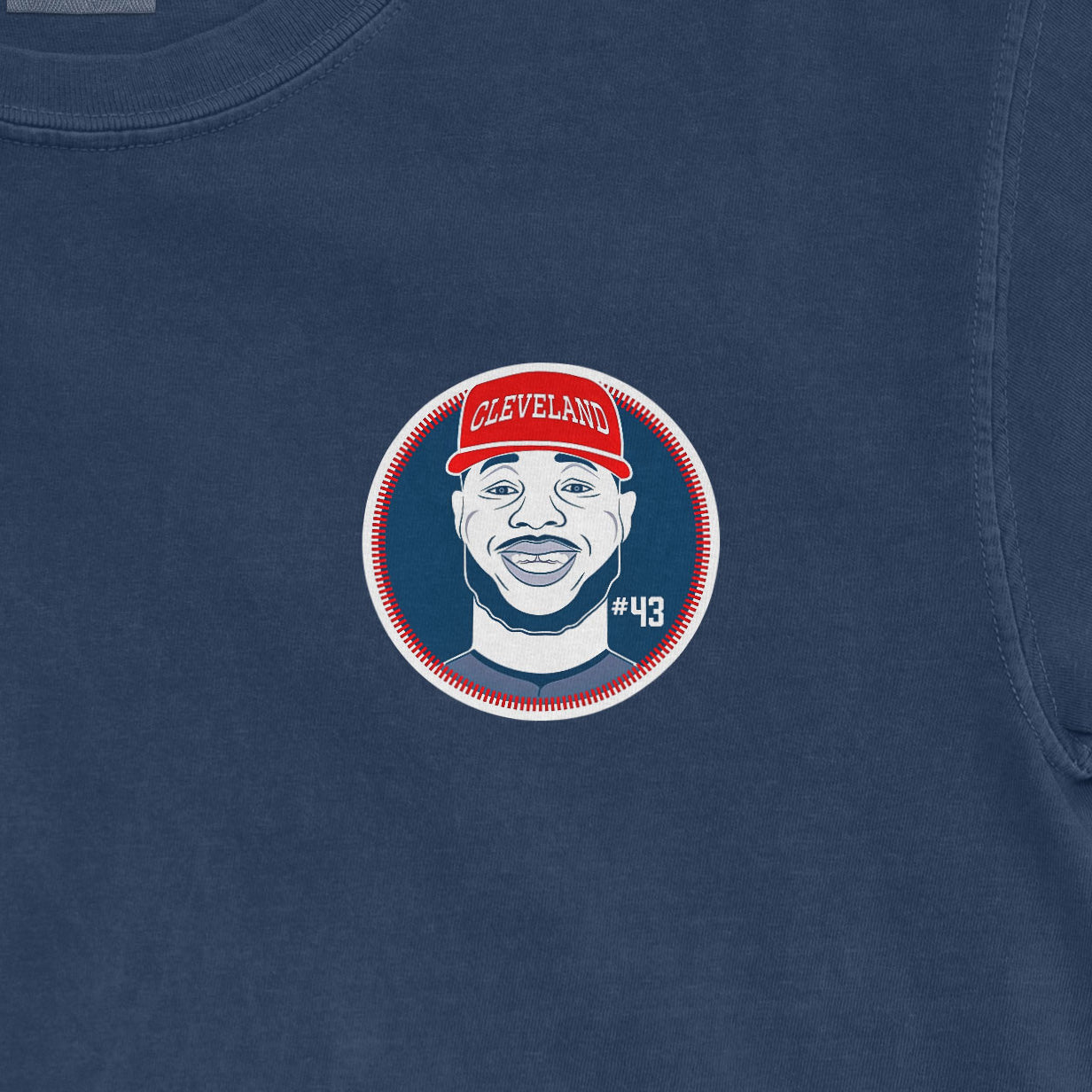 Close-up of a Comfort Colors tee featuring a graphic of a smiling man wearing a red Cleveland cap, with "#43" on a blue background.