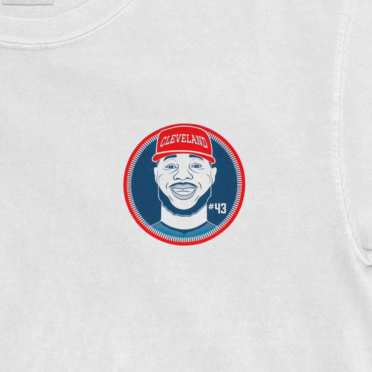 Close-up of a white Comfort Colors T-shirt featuring a graphic of a smiling man wearing a red Cleveland cap, with "#43" on the shirt.