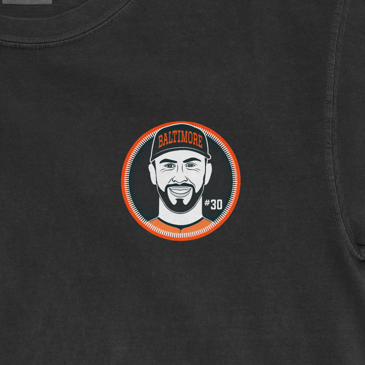 Close-up of a black Comfort Colors tee featuring a graphic of a smiling man with a beard, wearing a Baltimore cap, #30.