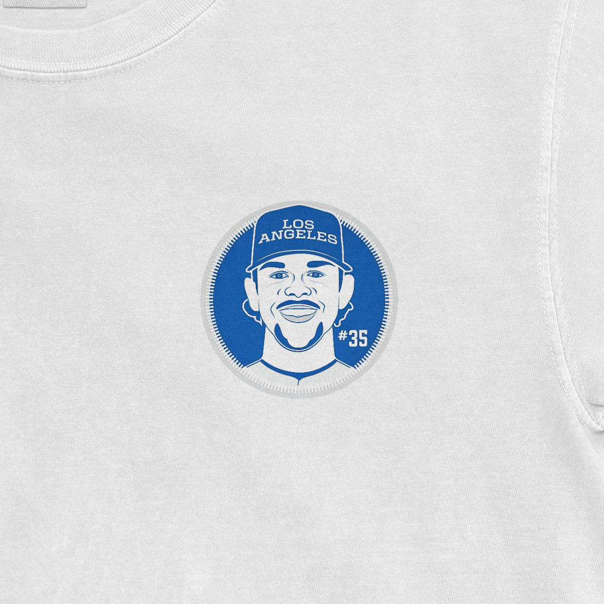 Close-up of a white Comfort Colors tee featuring a blue graphic of a smiling man wearing a "Los Angeles" cap, with "#35" on the side.
