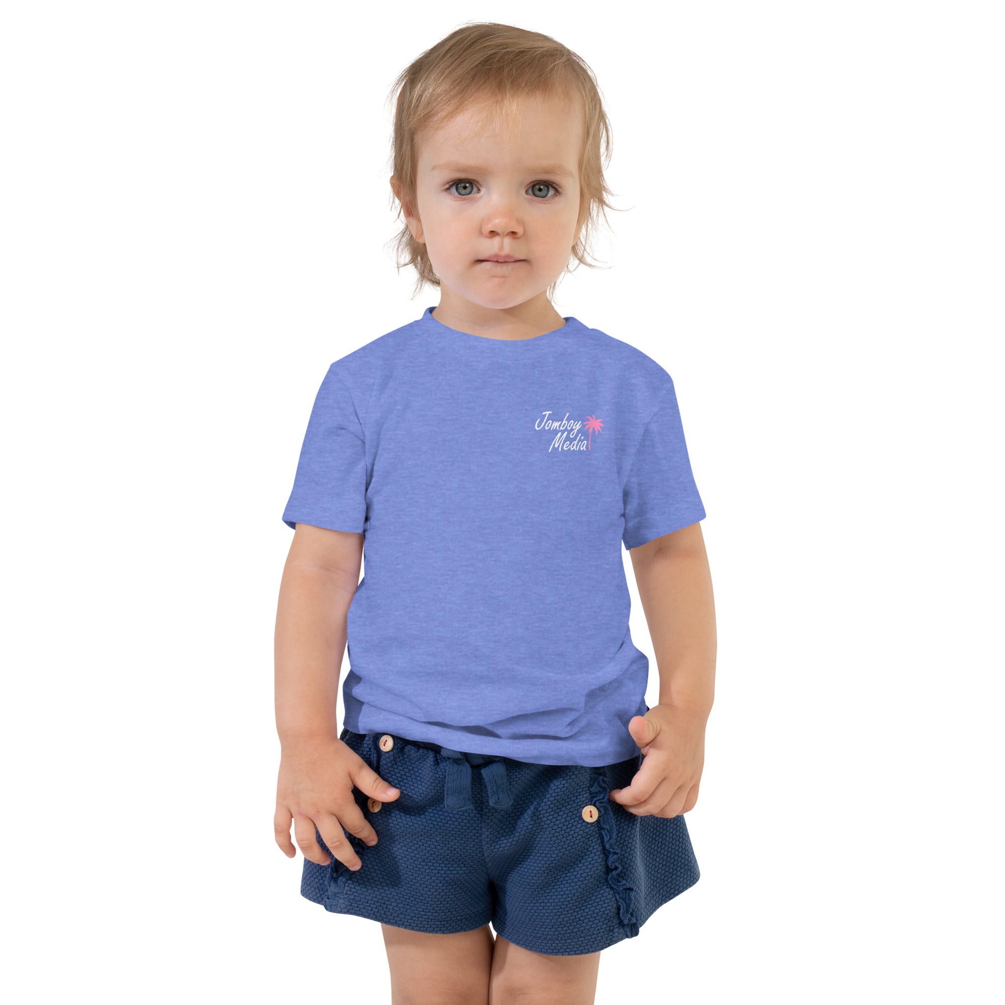 A young child with blonde hair and blue eyes wearing a blue "Jomboy Media" toddler t-shirt and navy shorts, standing against a white background.