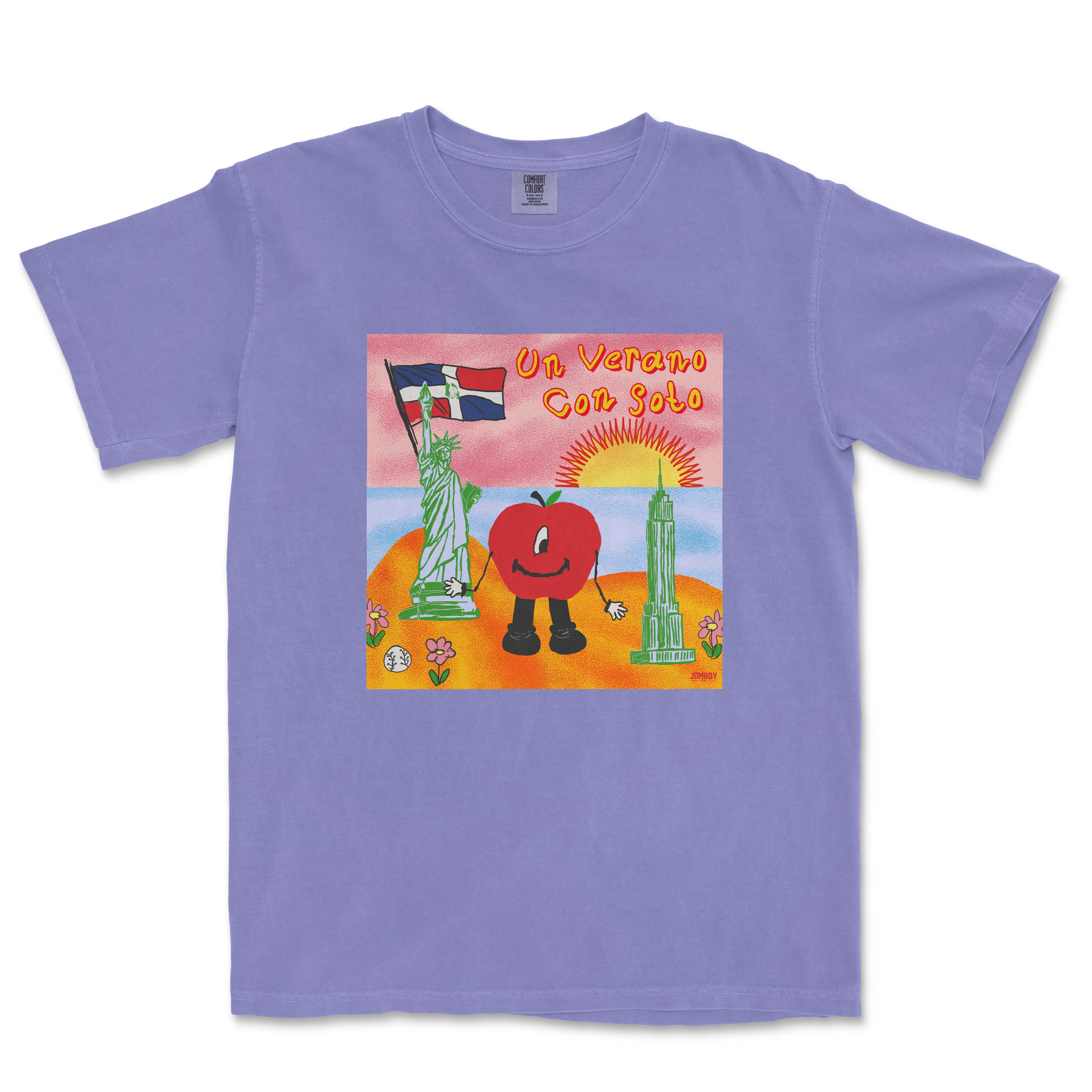 Lavender T-shirt featuring a colorful cartoon illustration of a tomato character with a sunset, Statue of Liberty, and Empire State Building, with "Un Verano Con Soto" text.