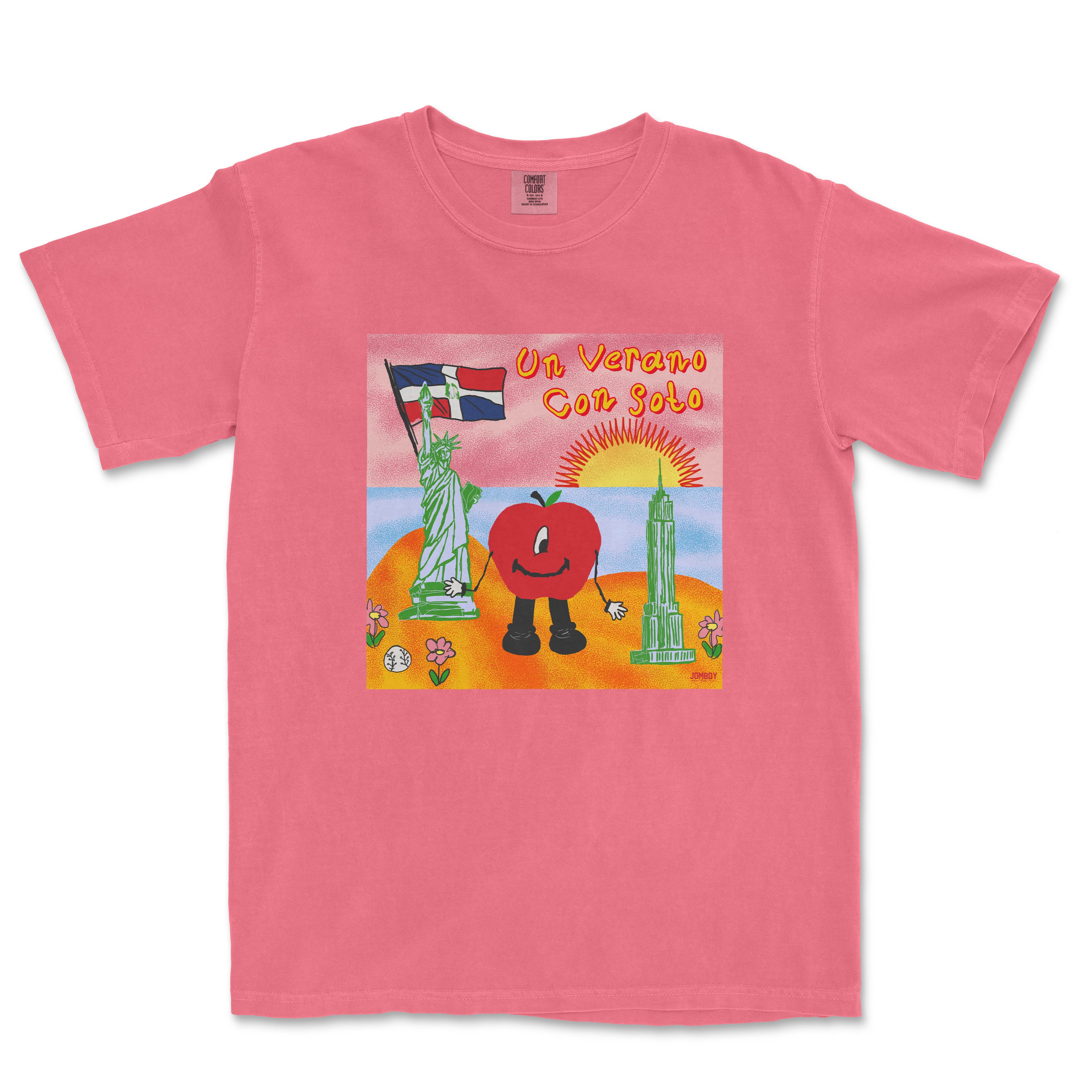 Pink T-shirt featuring a colorful cartoon illustration of a tomato character with arms and legs, holding a flag, with a sunset, Statue of Liberty, and skyscraper in the background, and the text "Un Verano Con Soto.