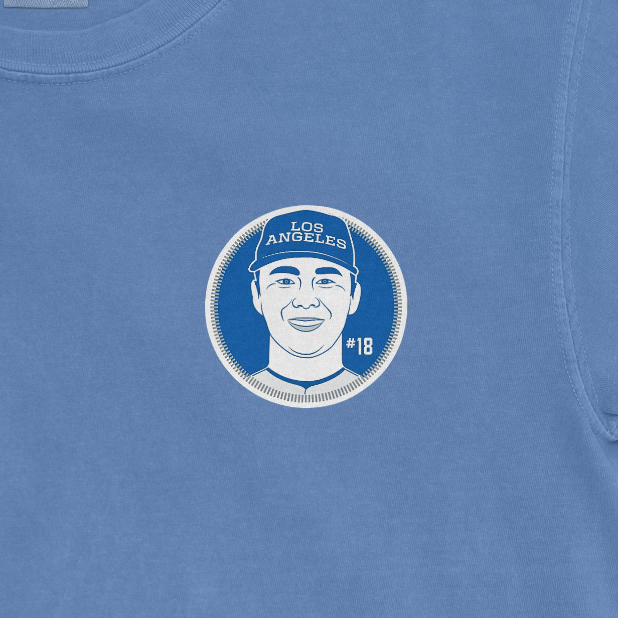Blue t-shirt featuring a graphic illustration of Yoshinobu Yamamoto with "LOS ANGELES" and "#18" printed around the face.