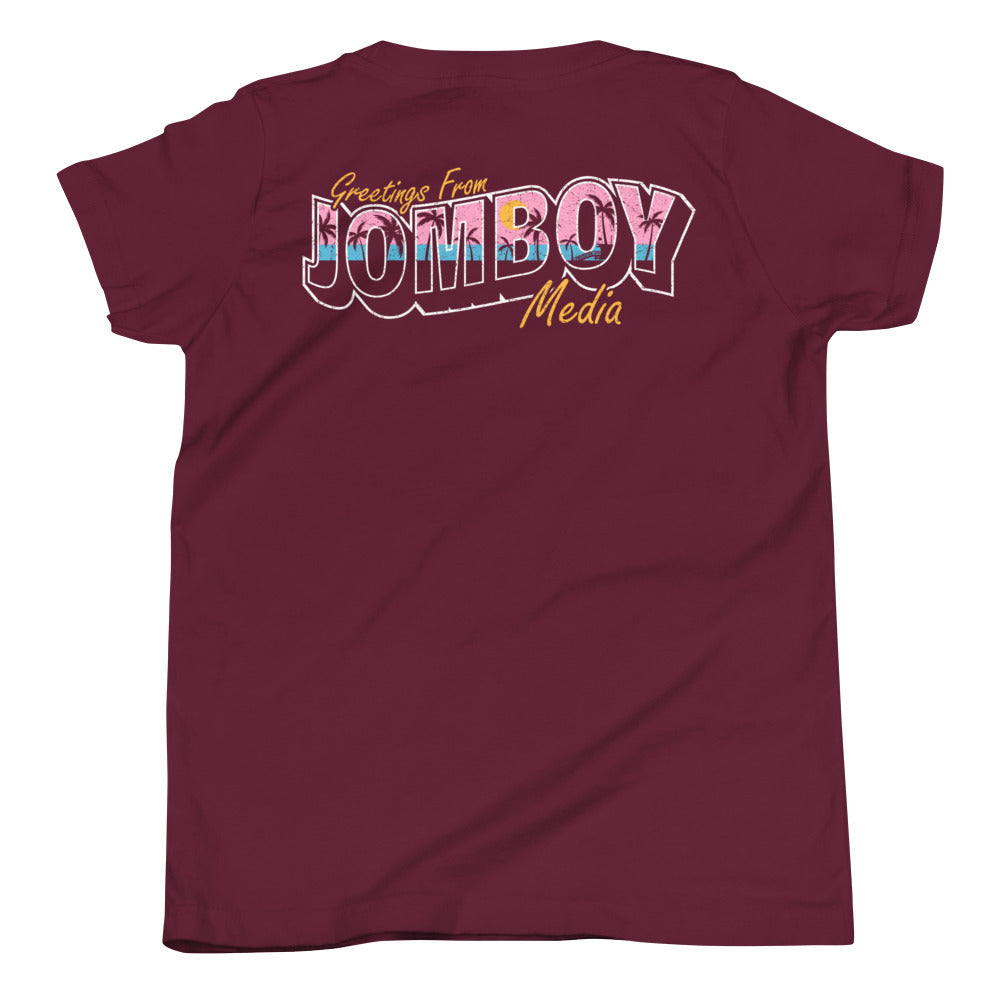 Back of a maroon youth T-shirt with colorful "Greetings from Jomboy Media" text featuring pink, blue, and yellow accents.