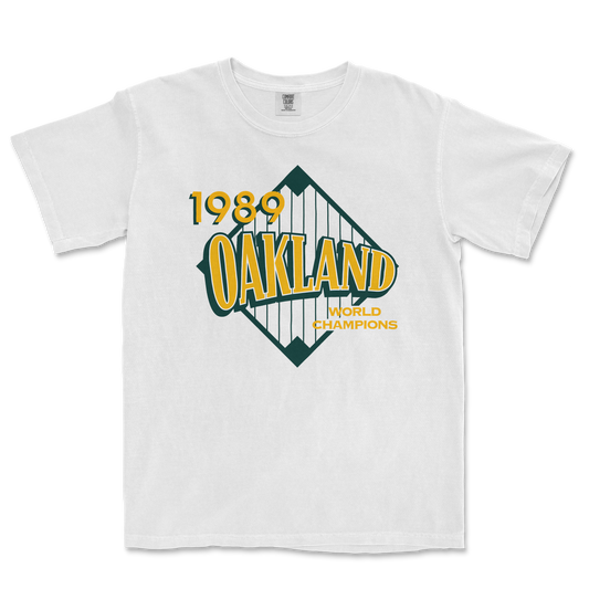 White Comfort Colors tee featuring a vintage Oakland 1989 World Champions graphic with yellow and green text and design.