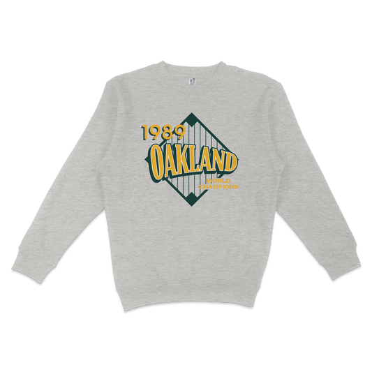 Gray crewneck sweatshirt featuring a vintage Oakland 1989 World Champions graphic with a bridge design and bold yellow and green text.