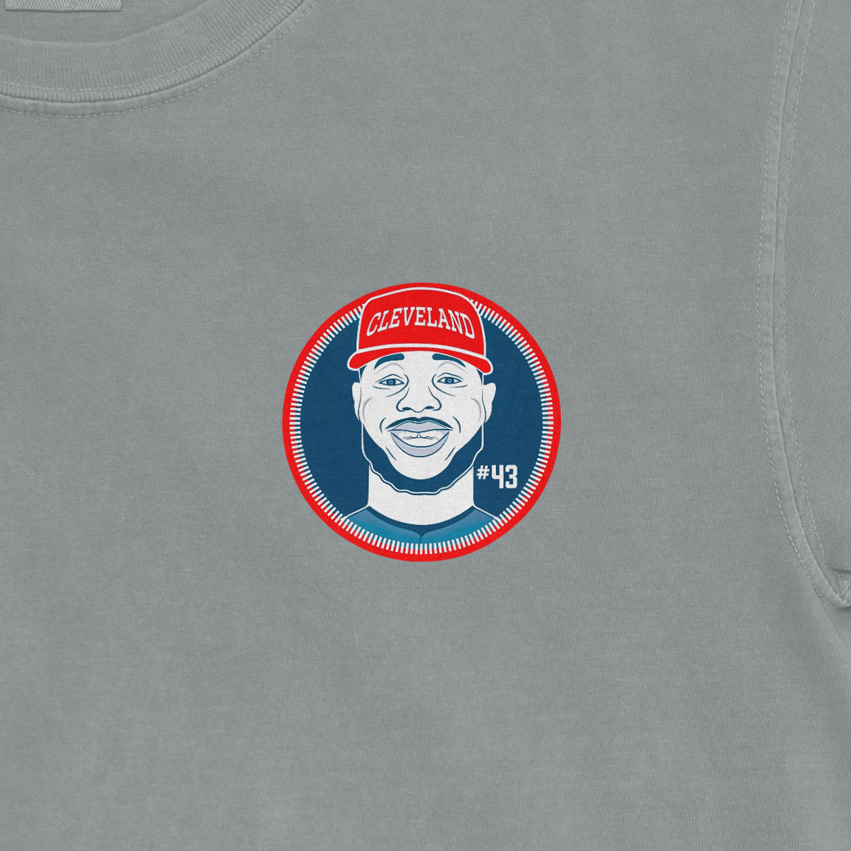 Close-up of a Comfort Colors tee featuring a graphic of a smiling man wearing a red Cleveland cap, with "#43" on a blue background.