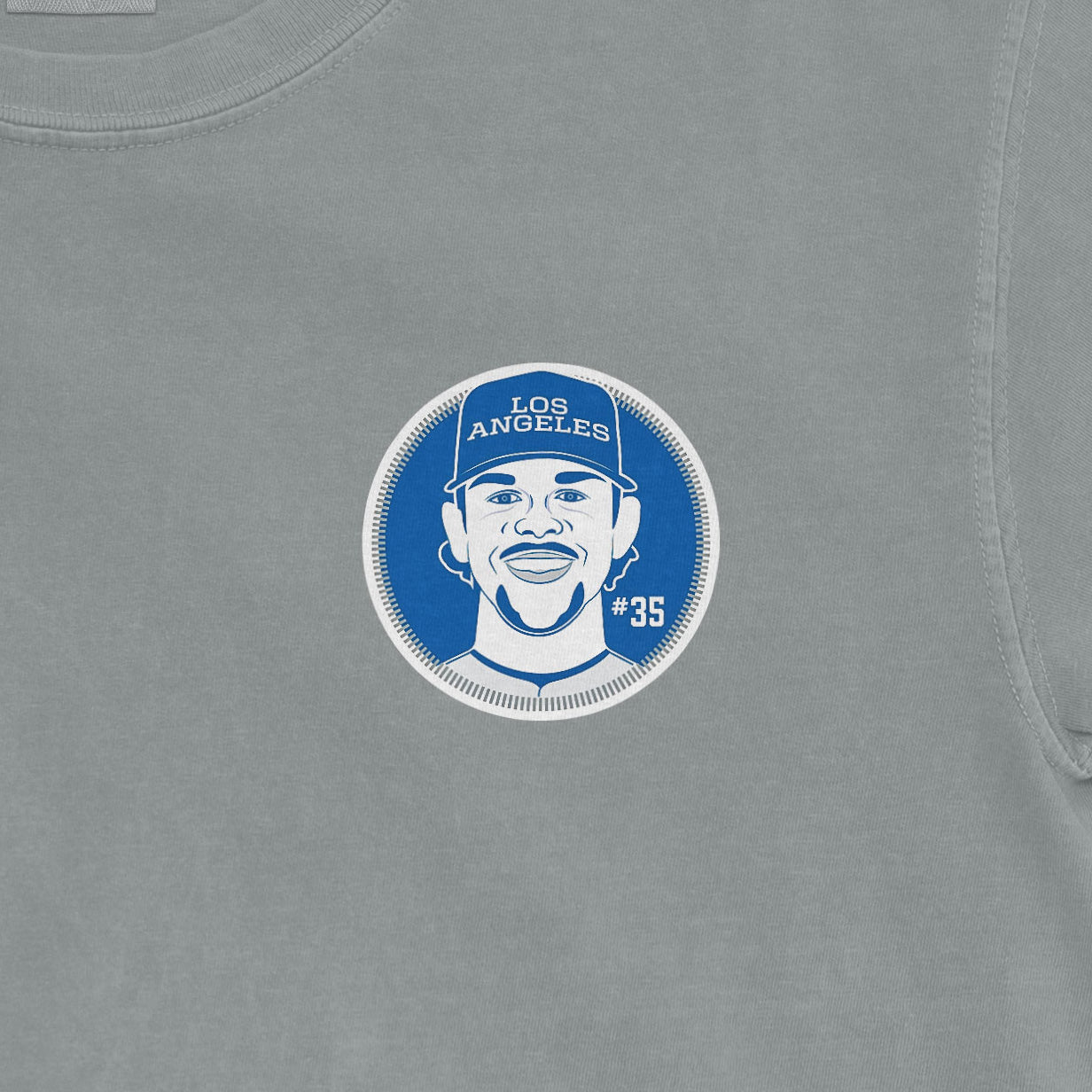Close-up of a Comfort Colors Gavin Stone Shirsey T-shirt featuring a blue and white graphic of a smiling man wearing a "Los Angeles" cap, with the number 35.