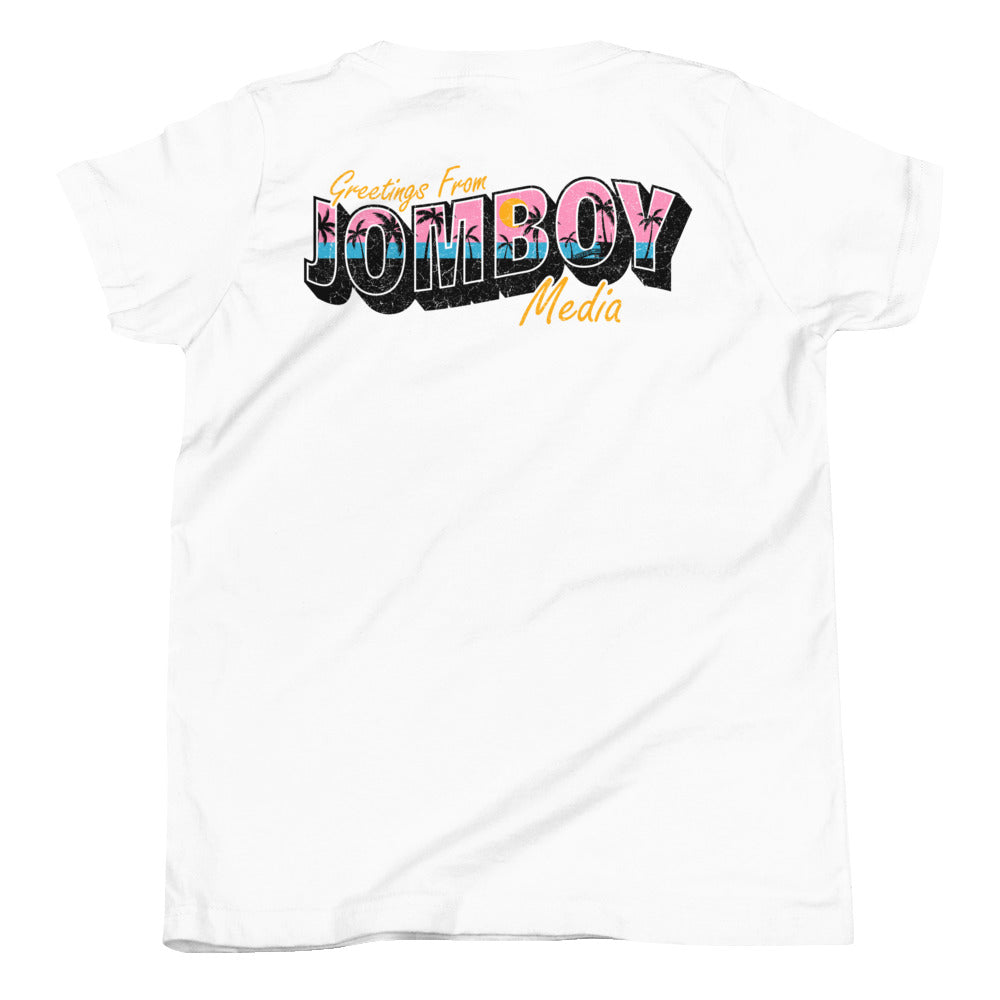 White youth T-shirt with colorful "Greetings from Jomboy Media" text, featuring pink, blue, black, and orange design elements.