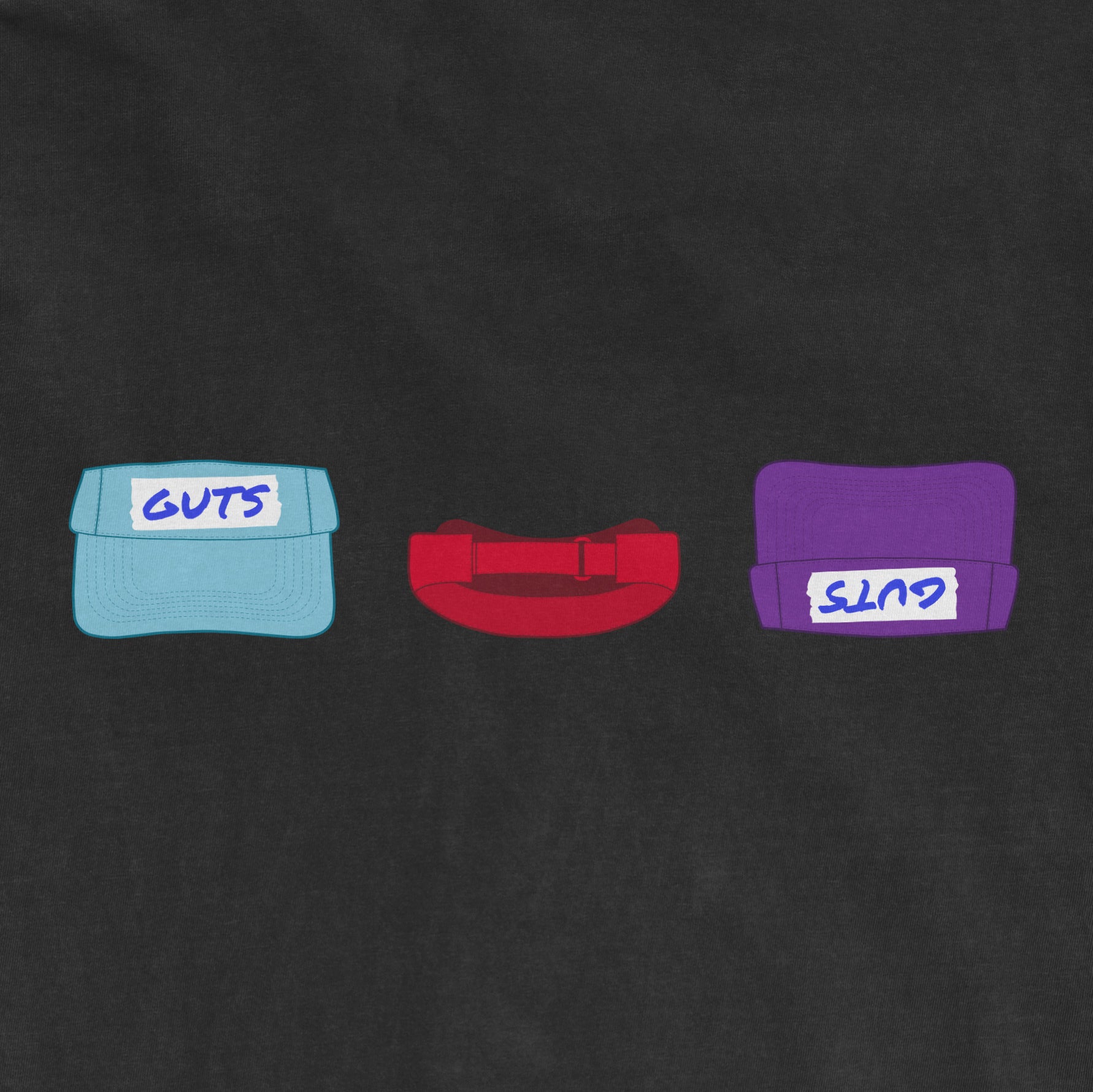 Three colorful hats with "GUTS" written on them, representing strength and resilience, on a dark fabric background.