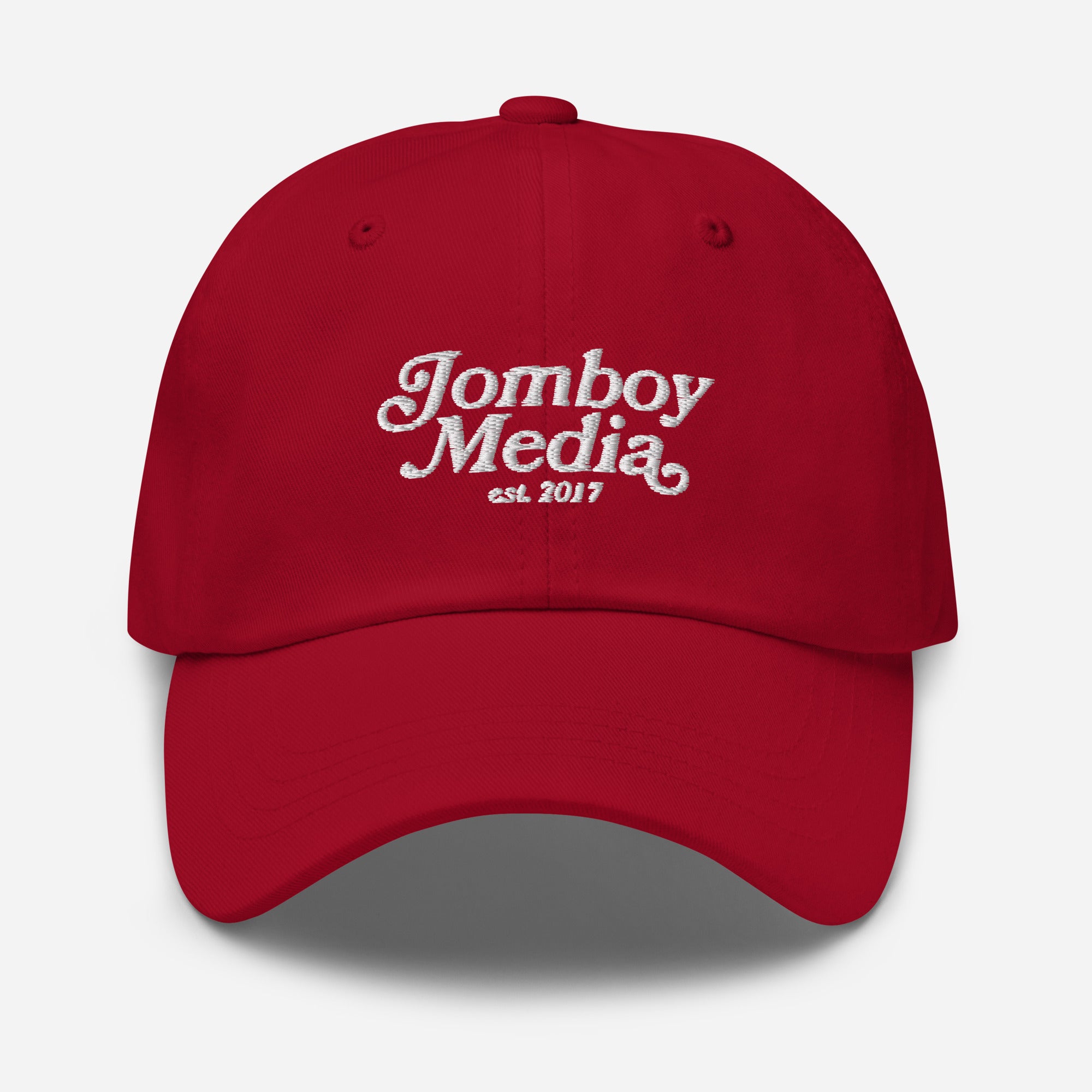 Red dad hat with white embroidered "Jomboy Media est. 2017" logo on front, curved brim, and adjustable strap.